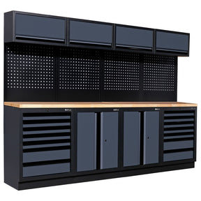 A modular workshop workbench from Bullram Werkstatteinrichtung, featuring a solid wooden worktop, dark grey cabinets and drawers for storage, a black perforated pegboard, and four matching overhead cabinets. This type of workshop furniture is available on Tools.de.